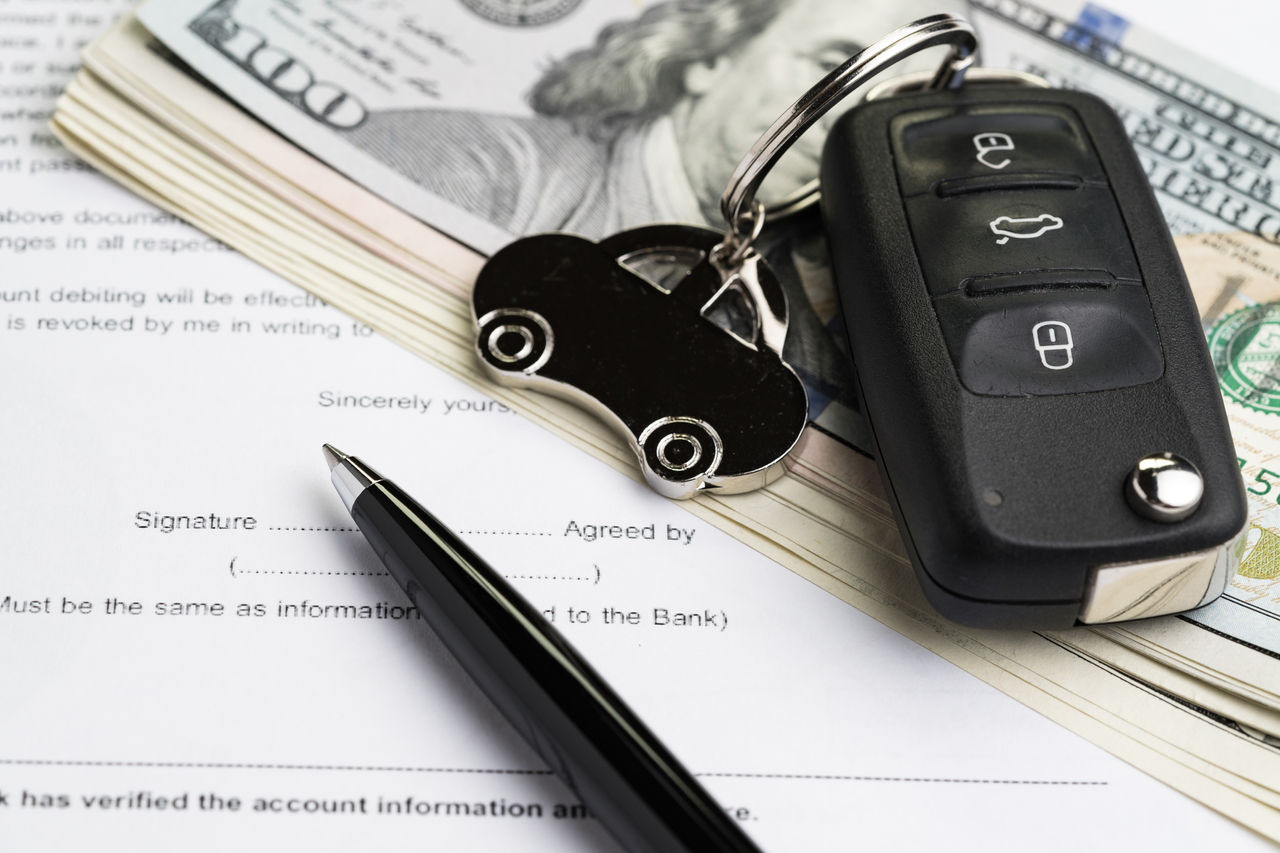 false Buy or sell car, purchase or rent automobile service with key with car keychain on pile of US Dollar banknotes money on printed contract paper and pen to sign, finance installment or debt awareness.