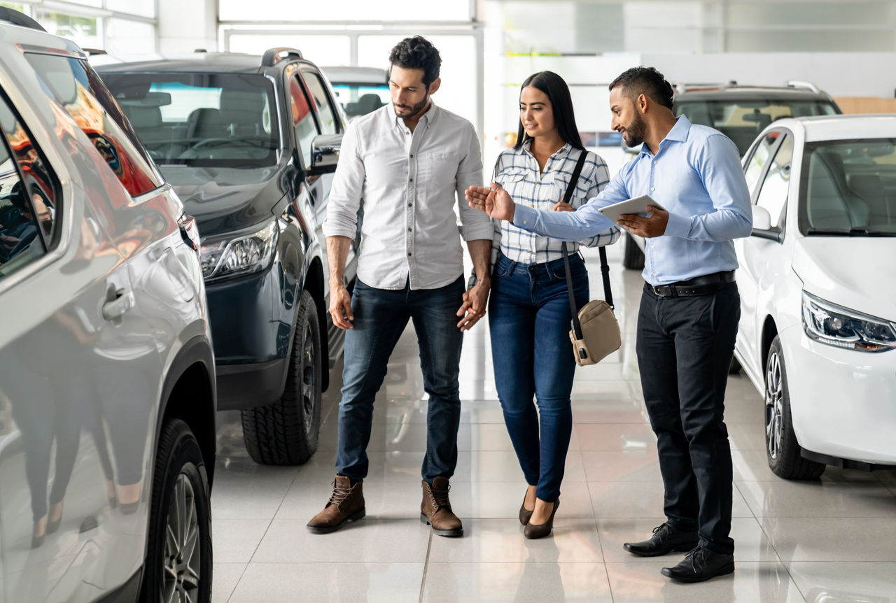 false Latin American salesman at the dealership showing a car to a couple interested in buying a vehicle - business concepts