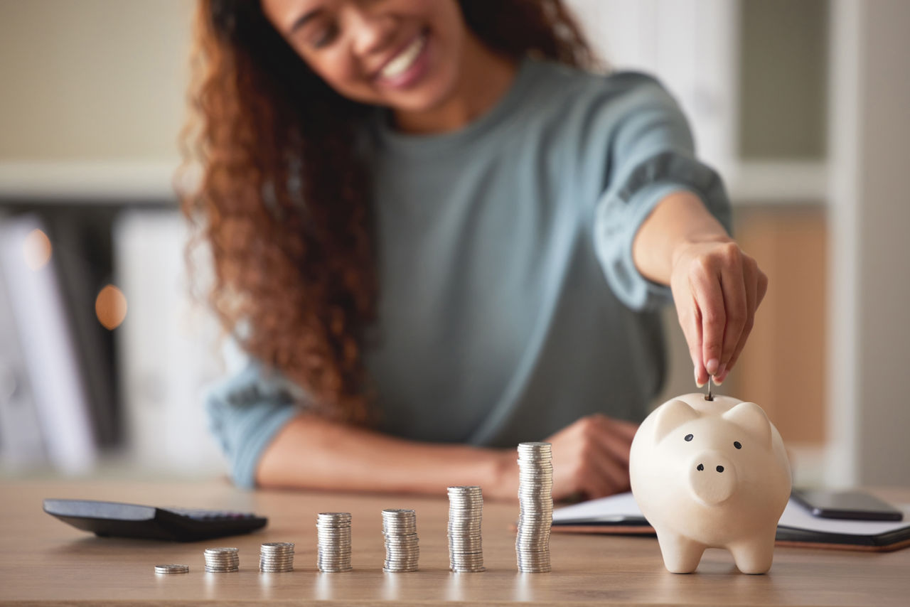 false Young african american woman money putting coins into a piggybank at home. Mixed race person counting coins while financial planning in her living room. Saving, investing and thinking about the future