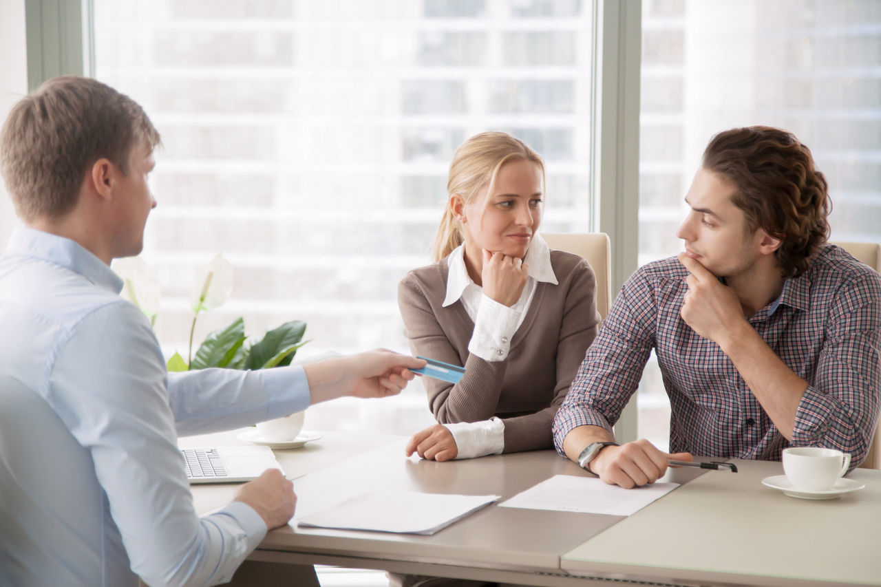 636613980 Bank consultant trying to convince clients to get a loan, offering credit card with high interest rate. Middle-class family sorting out finances and budget, not sure in the choice, looking doubtful