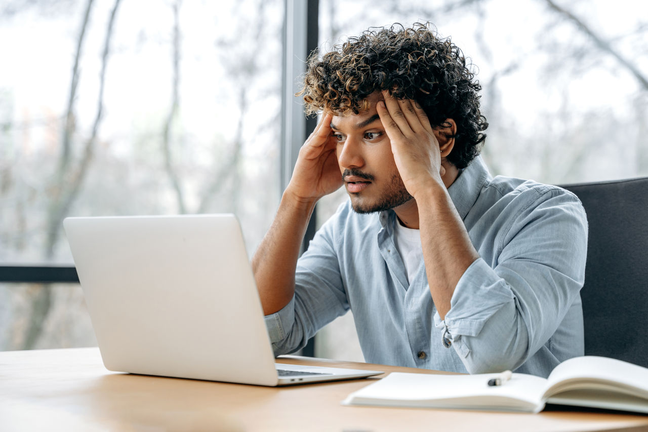 false Tired exhausted overworked indian office worker, creative manager, sitting at workplace holding his hands to his head, feeling stressed and tired from long work in laptop, needs a break, rest