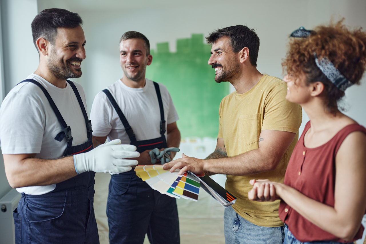 false Young happy couple talking to house painters while choosing colors during home renovation process.