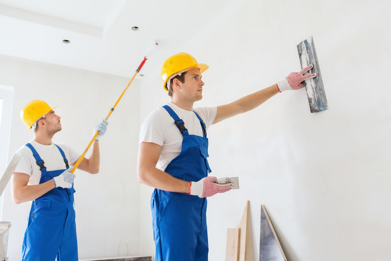 false business, building, teamwork and people concept - group of builders in hardhats with plastering tools indoors