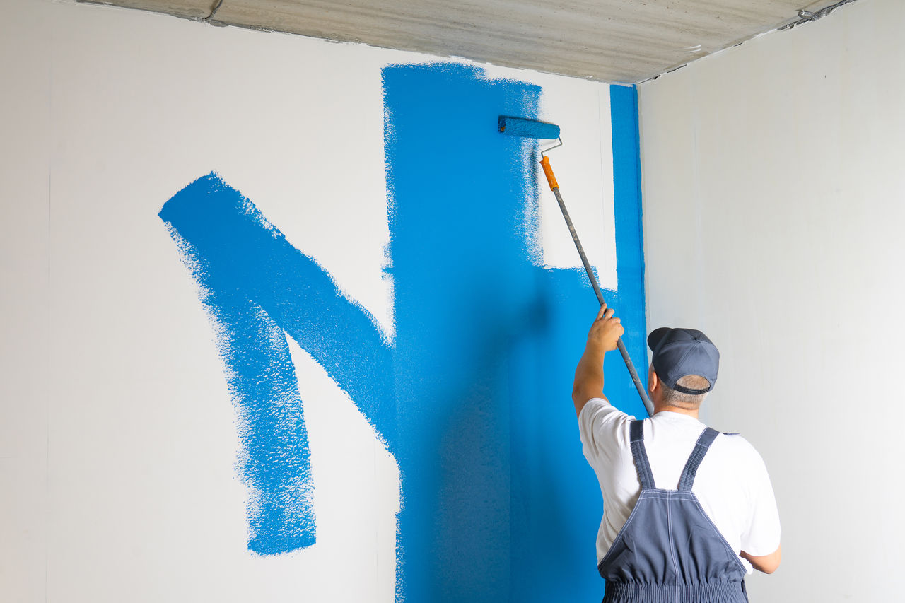 false Male painter painting a white wall with a roller in blue color renovations or construction concept