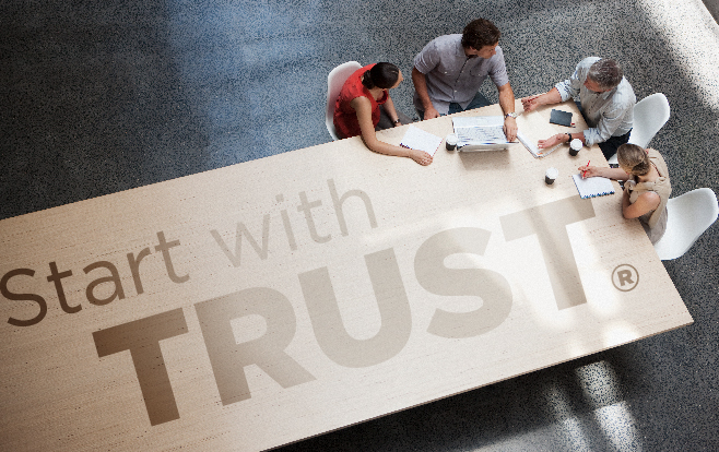 overlook of people sitting at a long table for a business meeting with "Start with Trust" overlay
